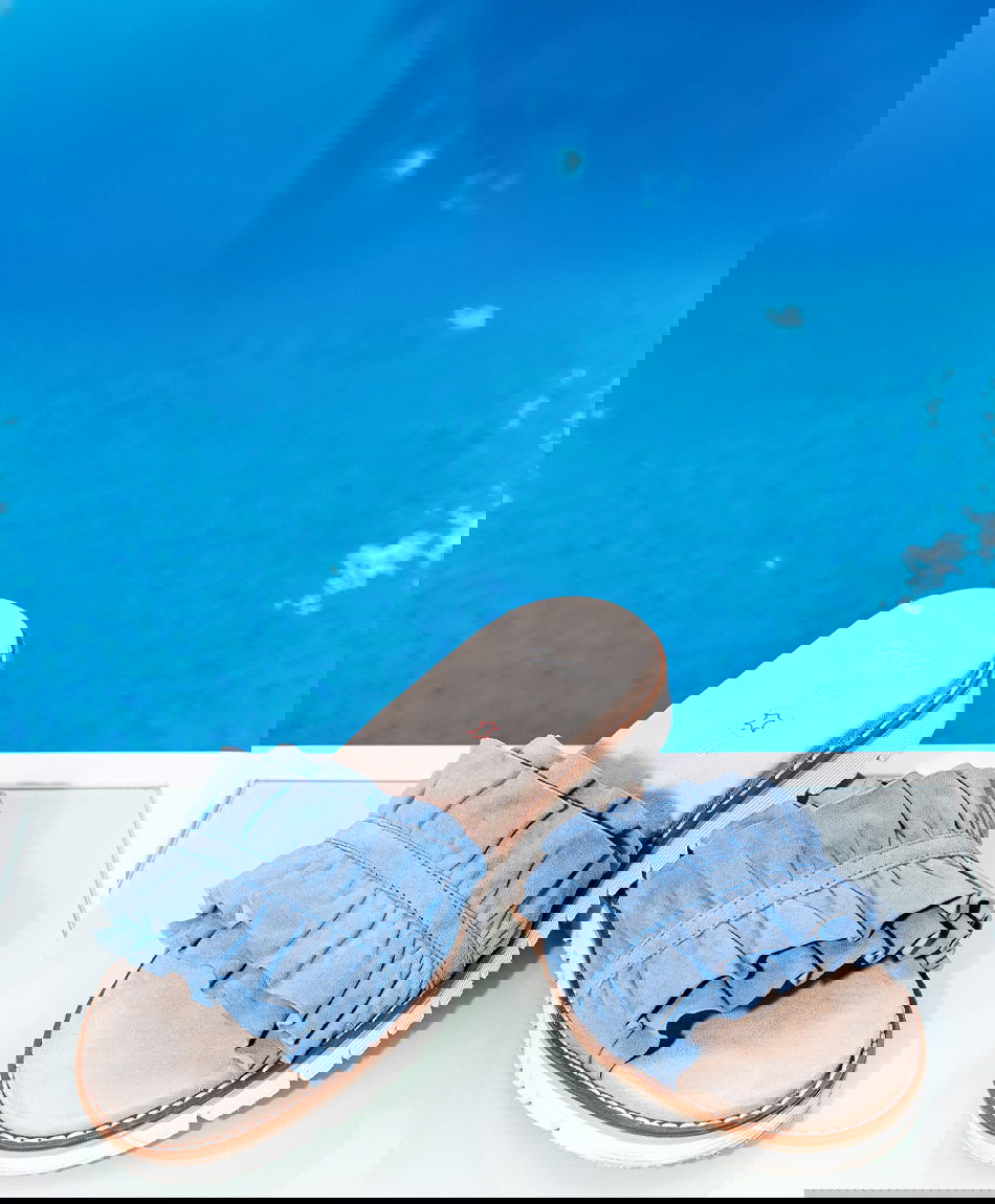 Blaue Rüschenpantoletten für Damen vor Poolhintergrund.